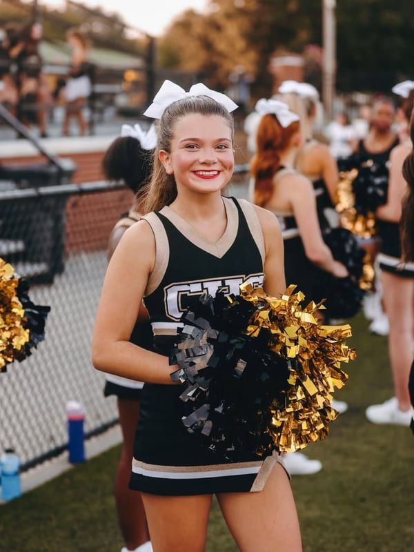 Caroline in her varsity cheer uniform with pom poms at a football game